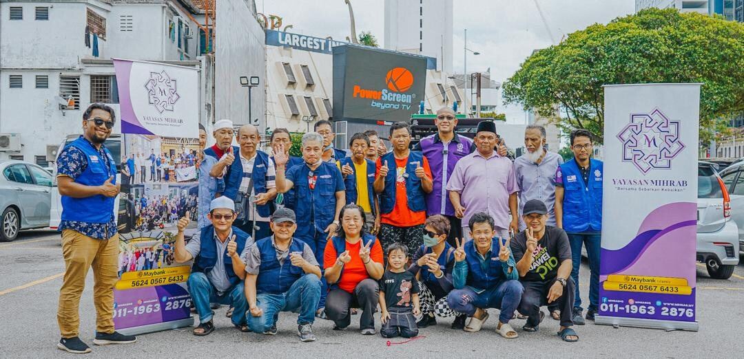 Sukarelawan dan komuniti bergambar bersama banner Yayasan Mihrab dalam program lapangan.
